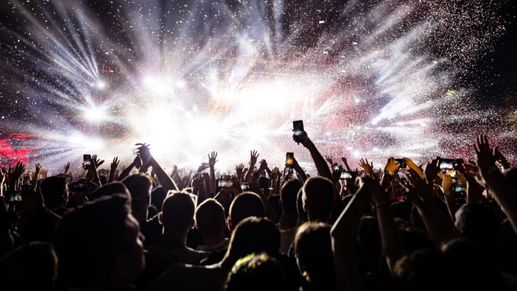 Drukke concertzaal waar mensen met telefoons presale FOMO ervaren bij exclusieve events.