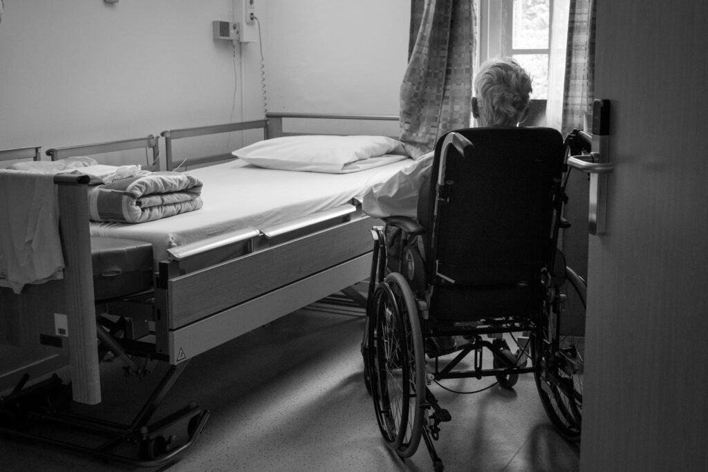 Oudere man in rolstoel kijkt uit het raam van een stille kamer in een instelling voor ouderenzorg.