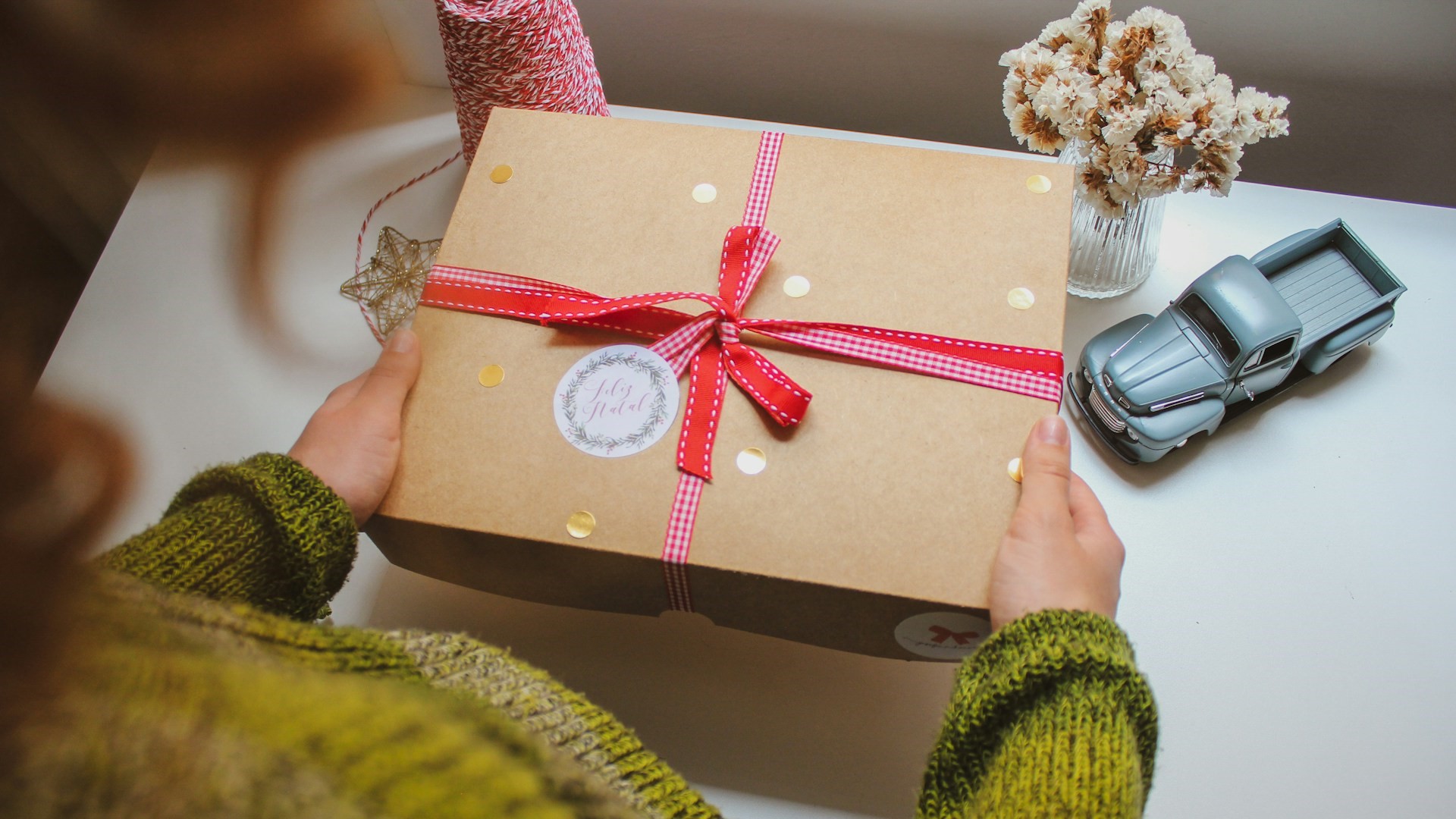 Persoon in groene trui houdt een eenvoudig cadeau vast met rood lint, passend bij het thema eenvoudig cadeau