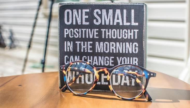 Quote met de tekst "One small positive thought in the morning can change your whole day", met bril op tafel