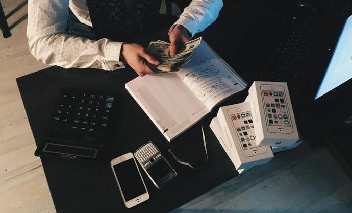 Man telt geld aan een donker bureau met telefoons, rekenmachine en notitieboek