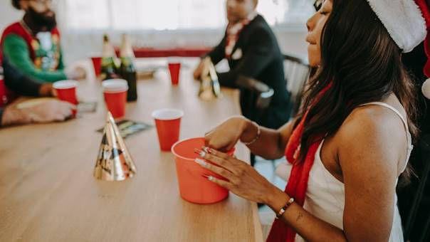 Vrouw met kerstoutfit pakt iets uit een rode pot tijdens een feestelijk eindejaarsmoment op het werk