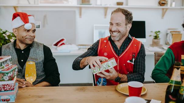 Lachende man in kersttrui opent een cadeau tijdens een feestelijke uitwisseling met collega’s