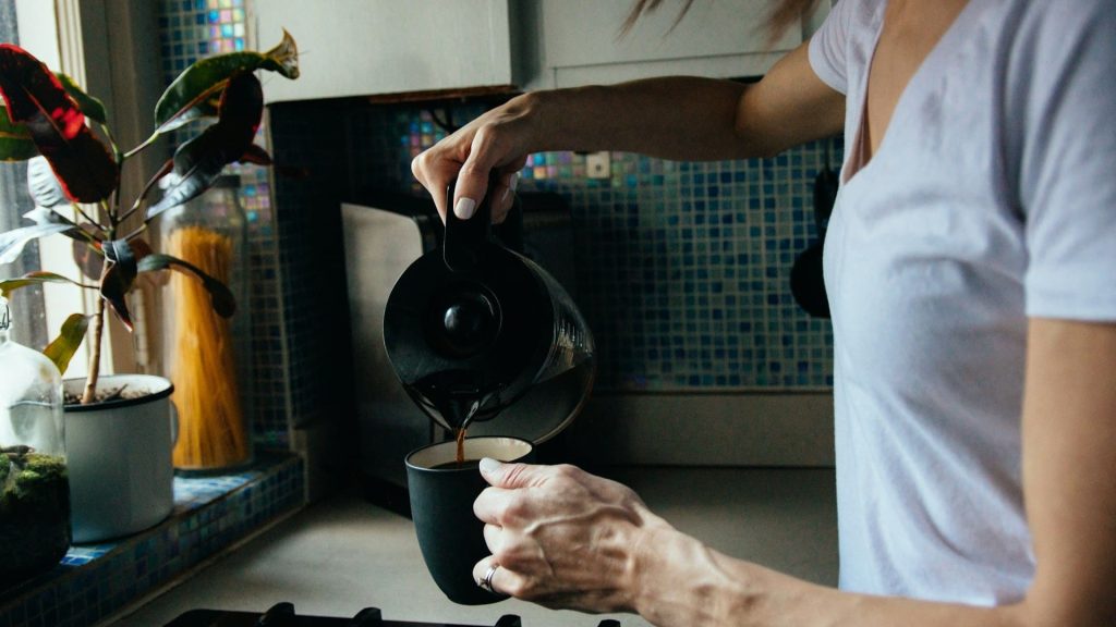 Vrouw schenkt koffie in mok als onderdeel van ochtendroutine, een voorbeeld van kracht van herhaling