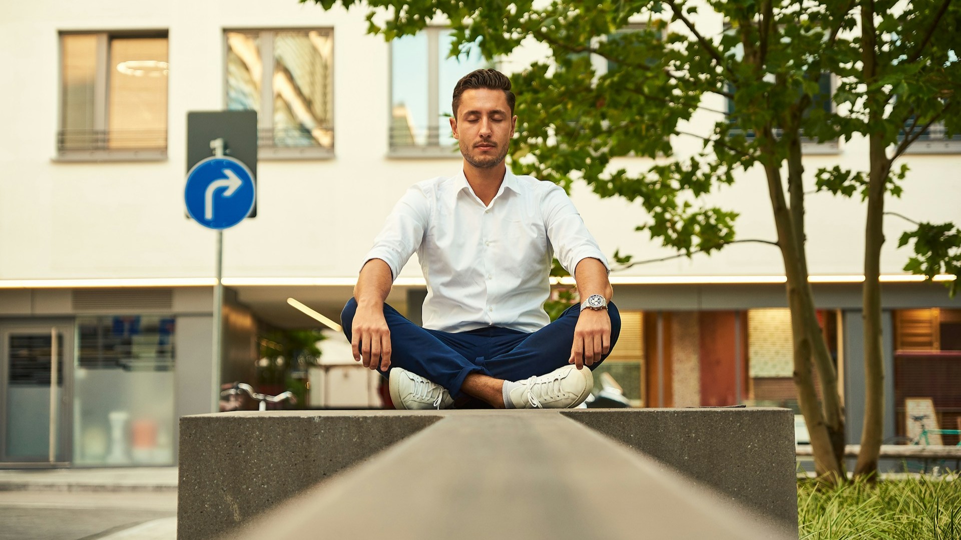 Man in stadskleding mediteert zittend in lotuspositie voor mentale rust te midden van stedelijke omgeving