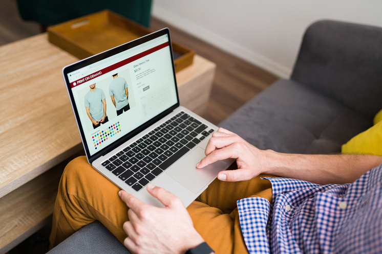 Man bekijkt kleding in een webshop op laptop tijdens online shoppen vanuit huis.