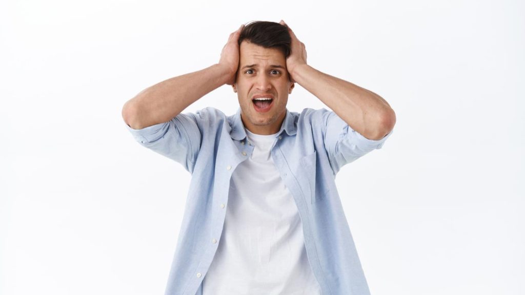 Man grijpt zijn hoofd in paniek, met geschrokken blik tegen witte achtergrond