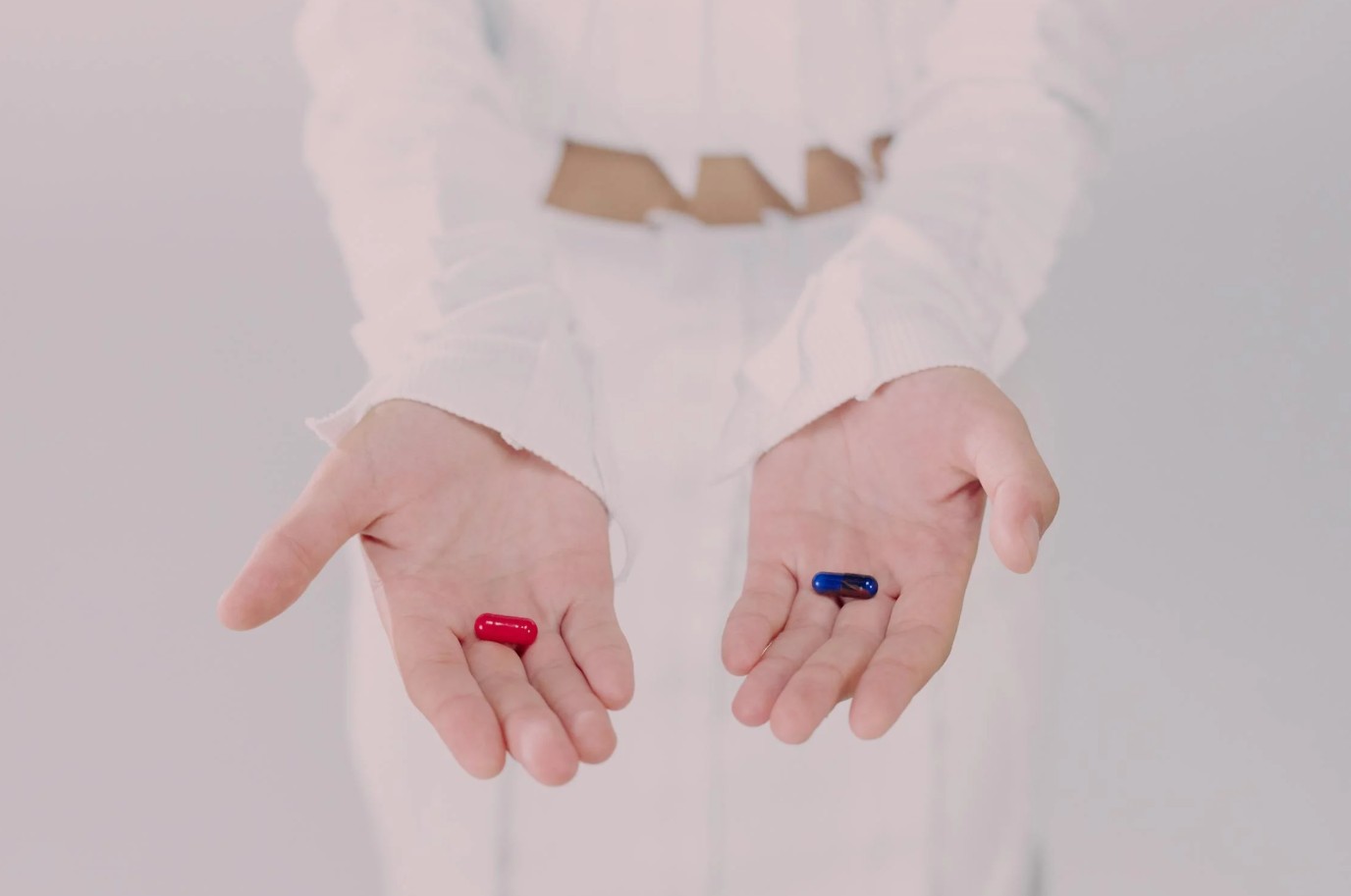 Twee open handen houden een rode en een blauwe capsulepil vast in een witte ruimte