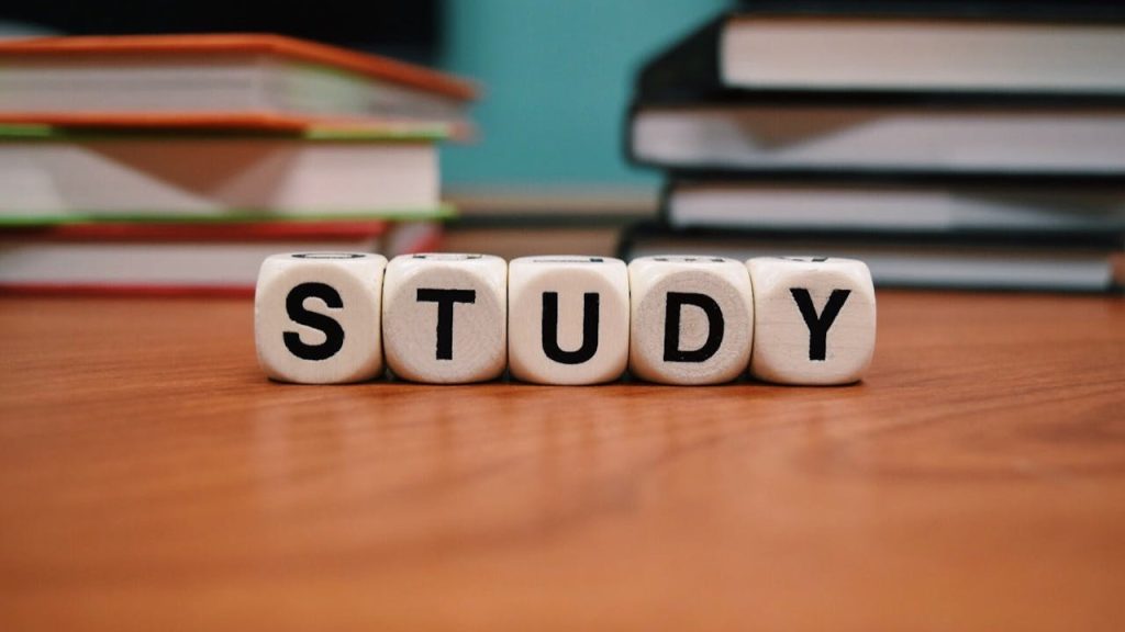 Houten blokjes met het woord "STUDY" op een bureau, met stapels boeken op de achtergrond – passend bij examens voorbereiden.
