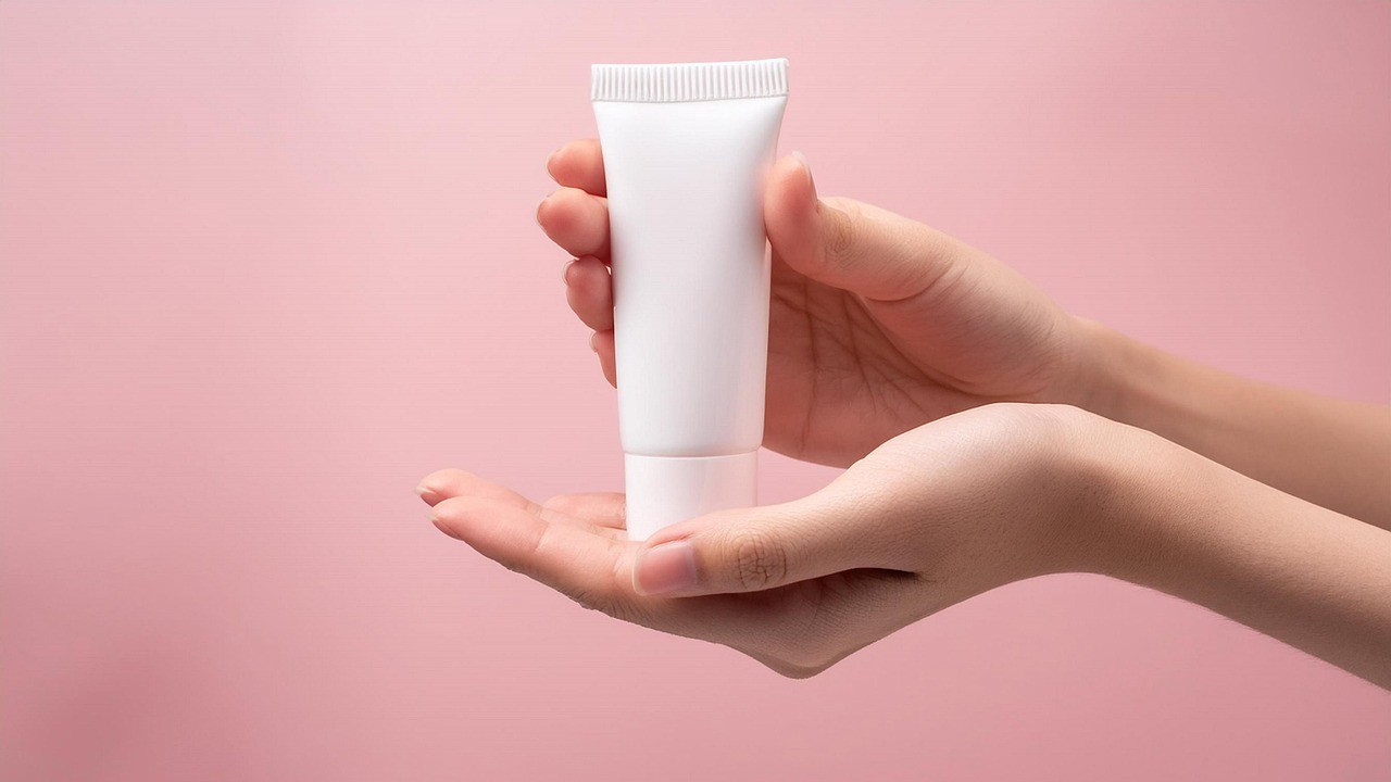 Handen houden een tube cr&egrave;me vast tegen een roze achtergrond, symbool voor beste voetverzorgingsproducten