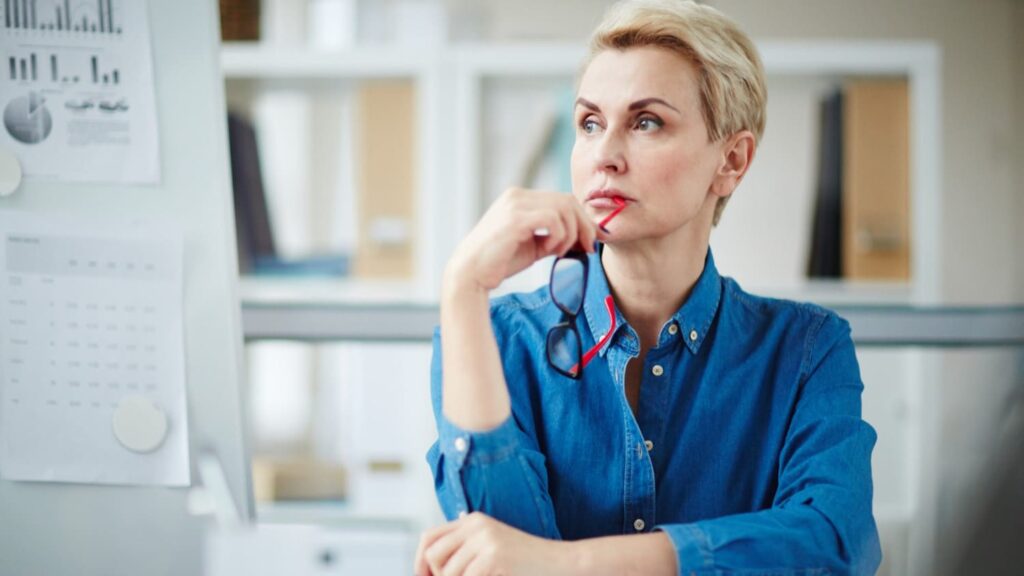 Vrouw in denim blouse denkt na over visuele branding tijdens werkoverleg op kantoor

